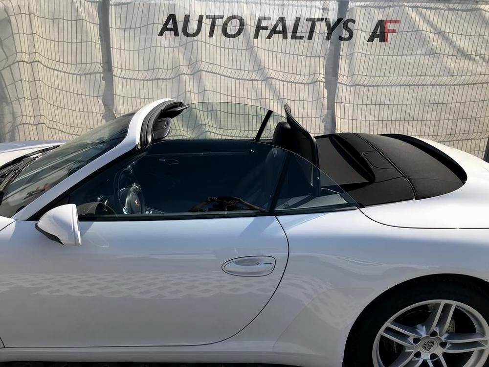 Pohled na boční část karoserie bílého Porsche 911 Carrera Cabriolet. Vůz má staženou střechu.